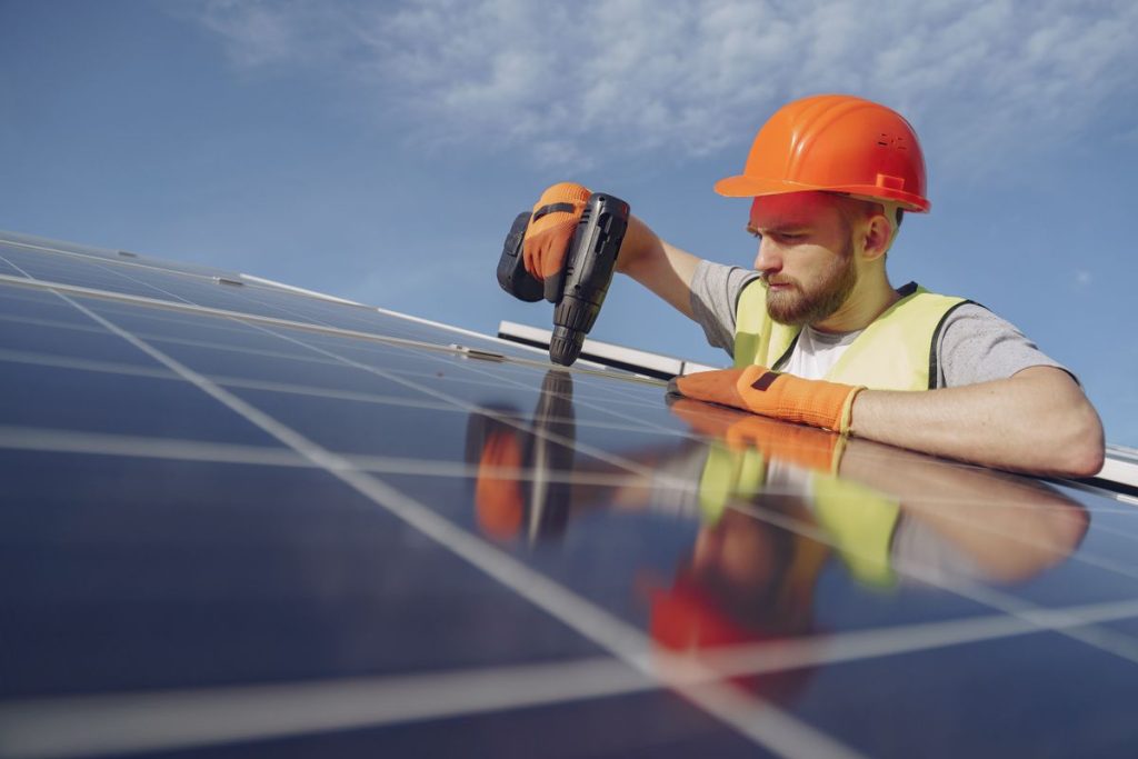 Electrician in a hard hat drilling a solar panel mount