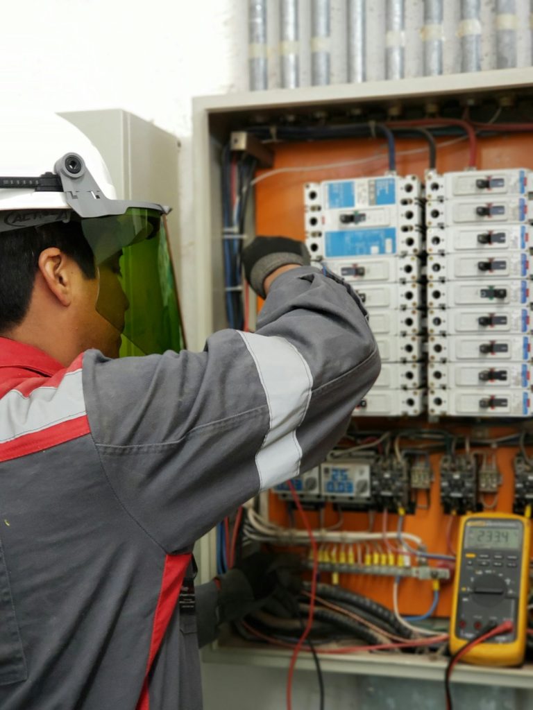 Electrician in a face shield testing an electrical distribution panel