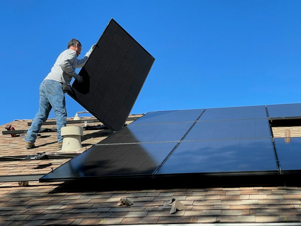 Installer placing a black solar panel on a shingled roof