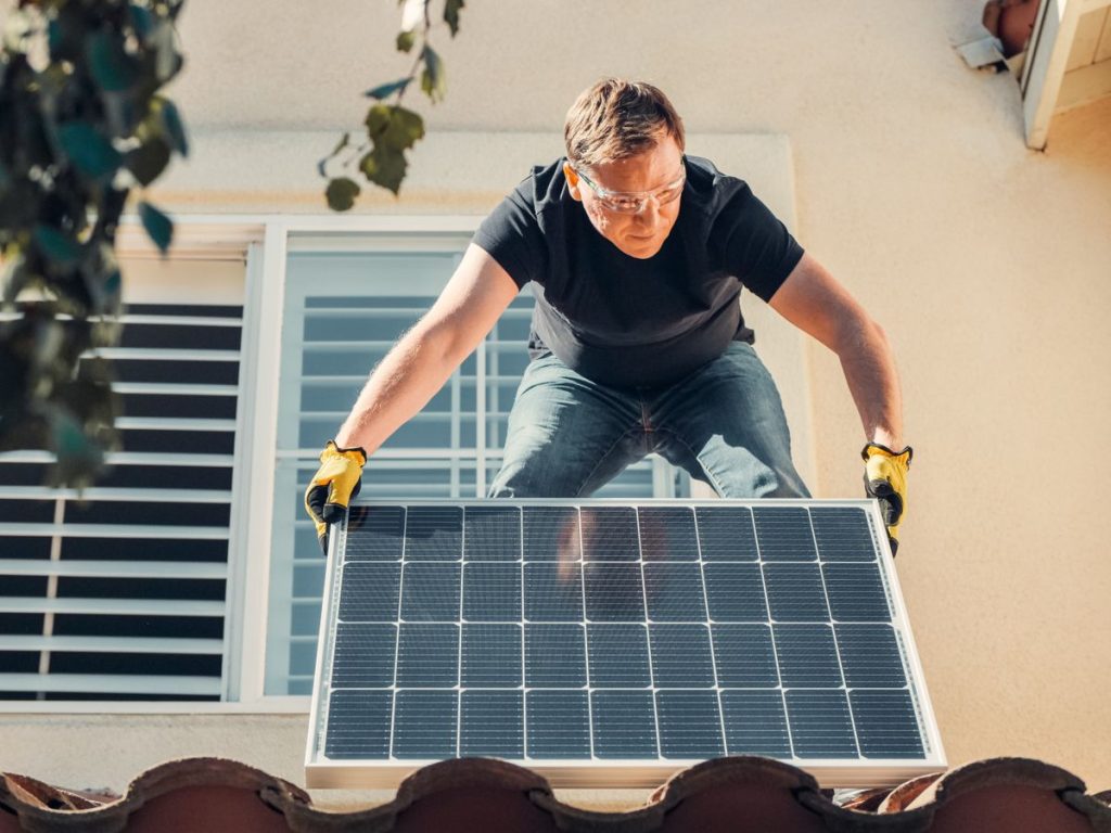 Solar installer in safety glasses mounting a panel on a house roof