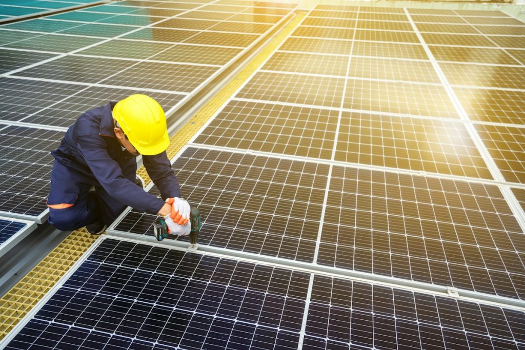 Technician in a yellow hard hat repairing a rooftop solar panel